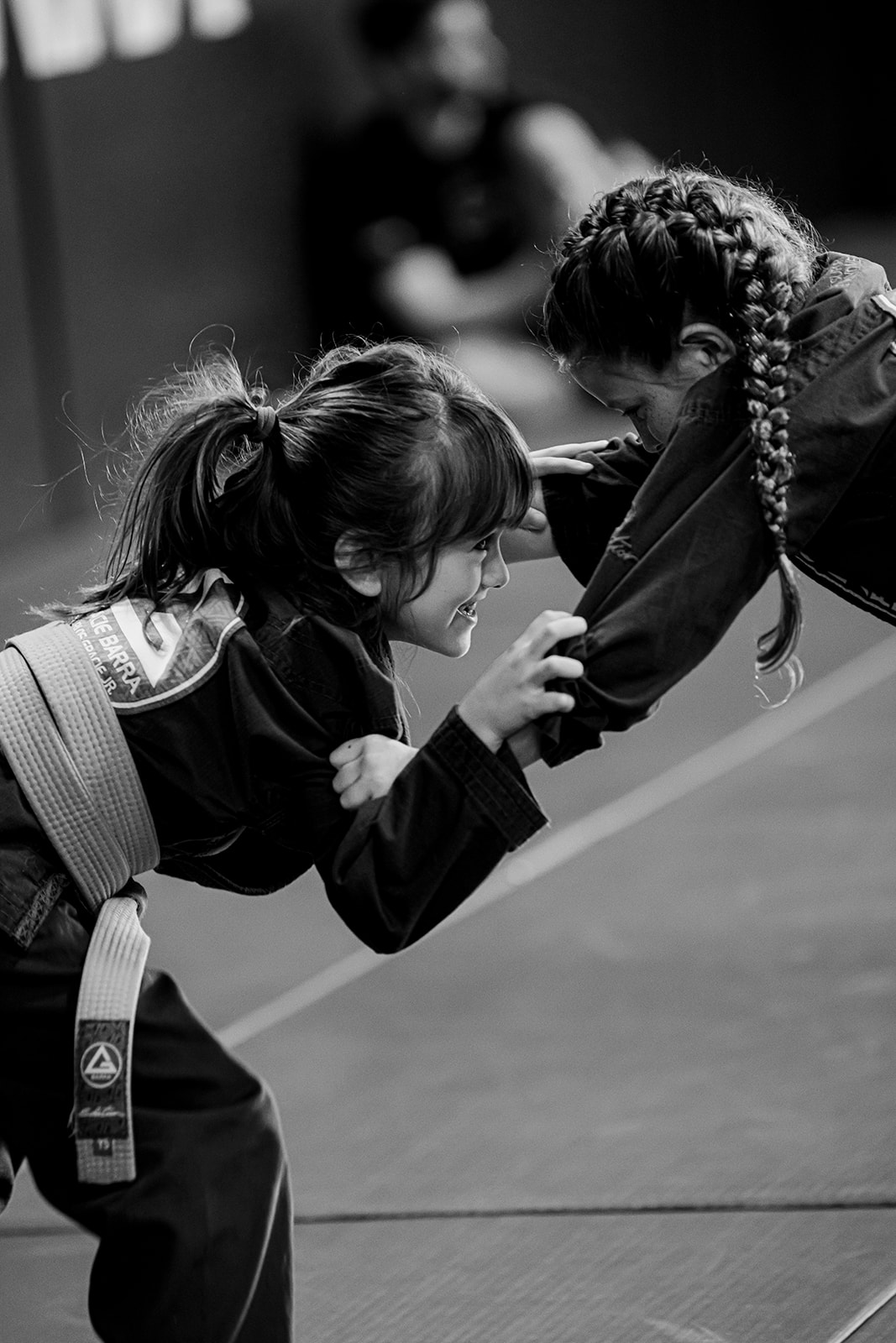 Two 8-year-old girls sparring in a kids’ BJJ class (black and white).